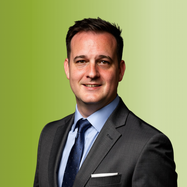 Person wearing a dark gray suit with a light blue dress shirt and navy tie, against a green gradient background.