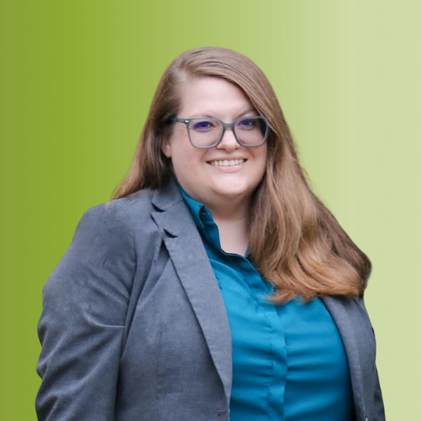 Person wearing a teal blouse under a gray blazer, with long straight hair, against a green gradient background.
